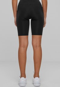 Pantalones cortos de ciclismo negros elásticos con una cinturilla de altura media, que presentan una textura suave y un diseño ajustado, combinados con zapatillas deportivas blancas.