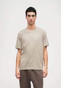 Beige bomullströja med avslappnad passform, korta ärmar och rund halsringning. Slät textur, minimalistisk design och utan synliga mönster eller detaljer.