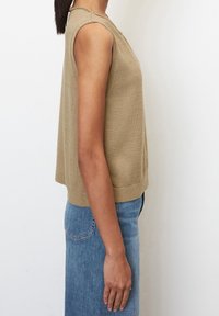 Beige stickad ärmlös topp med rund halsringning, som har en avslappnad passform och ribbad nederkant. Matchad med blå denimjeans.