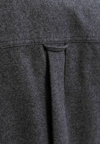 Tejido de lana gris oscuro con una textura sutil, que presenta un pliegue en la parte posterior y una costura a lo largo del borde superior.