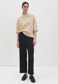 Beiger übergroßer Oberteil mit weiten Ärmeln, kombiniert mit schwarzen, weit geschnittenen Hosen. Schwarze Loafers komplettieren das Outfit. Einfaches, modernes Design.