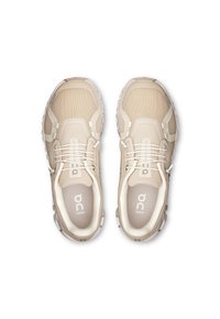 Baskets de sport beiges avec tige en mesh, semelle en caoutchouc et lacets élastiques. Présente un logo sur la languette et un col rembourré pour le confort.