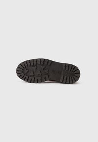 Suela de goma negra con un patrón de banda de rodadura resistente para agarre, logo en relieve "Marc O'Polo" y superficie texturizada para mayor durabilidad.
