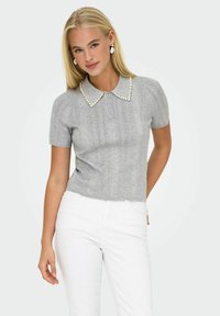Maglione polo corto grigio a maniche corte con motivo testurizzato e collo decorato con perle. I pantaloni bianchi completano l'outfit.