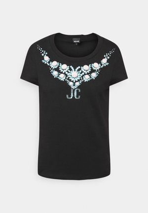 Czarny t-shirt z krótkim rękawem i okrągłym dekoltem, z niebiesko-różowym, klejnotopodobnym kwiatowym wzorem i inicjałami "JC" na piersi.