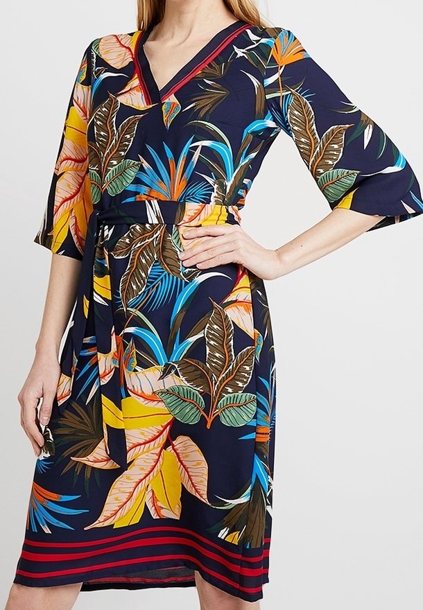 Blommig klänning med marinblå bakgrund, V-ringning, trekvarts ärmar med klockform och ett midjebälte med randig nederdel.