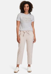 Lysegrå t-shirt med et prikket design, parret med beige, strukturerede, højtaljede bukser med bindebælte. Hvide sneakers fuldender looket.