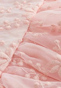 Tissu rose pâle transparent présentant des motifs délicats brodés de fleurs et de feuilles avec des détails de fils en relief texturés.