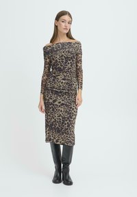 Abito con stampa leopardata, scollo a spalle scoperte, maniche lunghe trasparenti e texture arricciata. Indossato con stivali neri al ginocchio. Silhouette aderente.