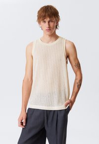 Lys beige ermeløs tank topp med ribbet tekstur, med en glatt crew-hals og en avslappet passform. Bært med mørkegrå bukser.