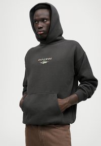 Tumehall kapuutsiga sviiter, millel on eesmine tasku ja rohelise aktsendiga tikitud "Ripcurl" logo. Pehme kangas ja mugav lõige.