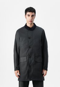 Manteau léger noir avec un col en laine, une fermeture à boutons sur le devant et deux poches avant. Le tissu semble texturé et lisse.