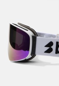 Gafas de esquí con un marco blanco curvado, lente de gradiente morado y acolchado suave. Cuenta con una cinta ajustable blanca con detalles del logo en negro.