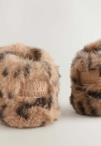 Chaussons bruns duveteux avec imprimé léopard, dotés d'un dessus texturé et d'un patch en cuir beige embossé avec "UN GRAND SOURIRE HEUREUX."