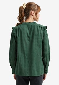 Green long-sleeve blouse with ruffled shoulders, featuring a textured pattern and buttoned cuffs. Back view showcases straight cut and neckline detail.