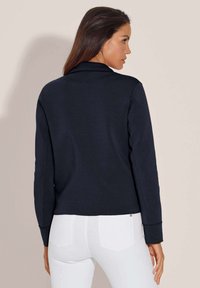 Marineblaue Sweatshirt mit tailliertem Design, langen Ärmeln und gerippten Bündchen. Glatte Textur mit leicht verkürztem Saum. Weiße Jeans sichtbar.