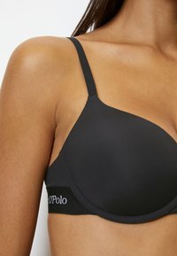 Sujetador negro con aros que presenta tejido suave, tirantes ajustables y una banda elástica con marca en la parte inferior.