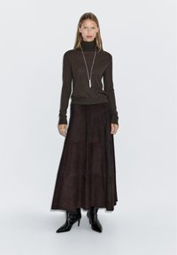 Brown turtleneck sweater paired with a long, dark brown suede maxi skirt and black pointed-toe ankle boots, featuring a minimalist silver necklace.
