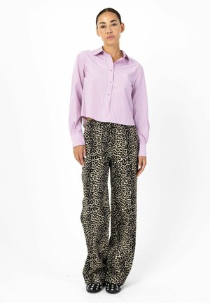 Gekürztes rosa-weiß gestreiftes Hemd mit Knopfverschluss, kombiniert mit weit geschnittenen Leopardenmusterhosen. Schwarze Akzent-Schuhe mit Nieten.