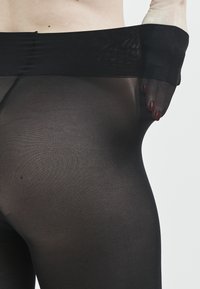 Sorte, gennemsigtige leggings med en blød, strækbar talje. Stof er glat og semi-gennemsigtigt, så huden viser sig nedenunder.