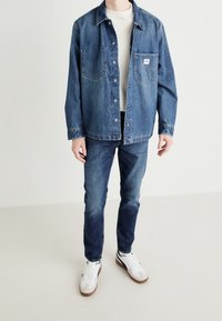 Farkku takki kahdella rintataskulla, sininen väri, rento istuvuus. Yhdistetty tummansinisiin booty-punaisiin farkkuihin ja valkoisiin lenkkarit, joissa on ruskeat pohjat.