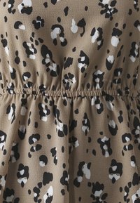 Tessuto beige con motivo leopardato in bianco e nero, caratterizzato da una vita elastica arricciata che crea leggere pieghe.