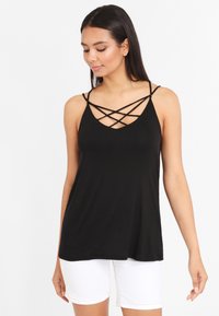 Black tank top with a V-neck and crisscross strap detail. Made from smooth fabric, it has a relaxed fit, paired with white shorts.