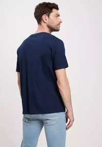 Granatowa bawełniana koszulka z okrągłym dekoltem i krótkimi rękawami, przedstawiona z tyłu, charakteryzująca się luźnym krojem i brakiem widocznych grafik.