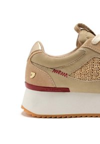 Sneaker beige con un lato tessuto testurizzato, dettagli in suede e una suola piatta bianca. Presenta cuciture rosse e un piccolo logo sul lato.