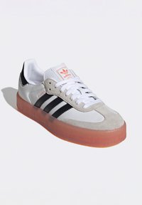 Sneakers Adidas Samba w białej, szarej i czarnej skórze z przezroczystą pomarańczową gumową podeszwą; posiadają trzy czarne paski i białe sznurowadła.