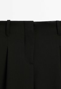 Gros plan sur la ceinture d'un pantalon noir avec des passants de ceinture et une couture de fermeture frontale dissimulée.