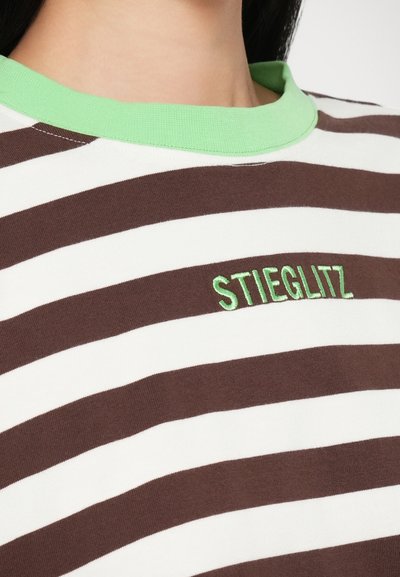 Pruun ja valge triibuline T-särk rohelise soonikkoega kaelas. Rinnal on rohelise värviga broderitud tekst "STIEGLITZ".