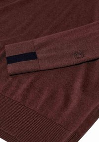 Bordo pleteni pulover s rebrastim manžetama, koji ima mornarsko plavu prugu na manžetama i mali detalj loga izvezen blizu izreza. 