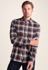 Checkered button-up shirt featuring navy, white, and orange plaid pattern. Long sleeves, collar, and patch pocket on the left side.