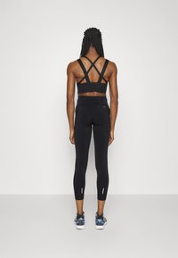 Črn športni modrček z križnimi naramnicami; črne pajkice z visoko pasom, ki imajo poudarjene črte na robu; obute črne in modre tene.