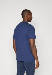 Marineblå bomulds T-shirt med korte ærmer og rund hals, glat tekstur; vist fra bagsiden, hængende løst ved taljen.