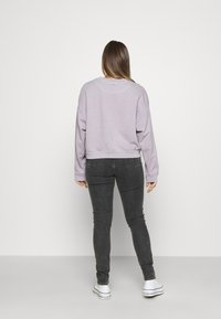 Felpa cropped lilac con spalle cadenti, orlo a costine e tessuto strutturato. Abbinata a jeans skinny neri e sneakers bianche.