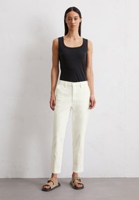 Top negro sin mangas, pantalones crema de corte recto y sandalias marrones con detalle de hebilla. Tejido suave y diseño clásico.