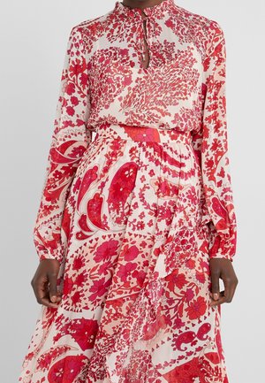 Ensemble blouse à manches longues et jupe avec motifs floraux et cachemire roses et rouges sur fond blanc, avec un col montant et un détail de lien en forme de trou de serrure.