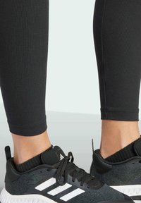 Leggings negras acanaladas combinadas con zapatillas deportivas negras y grises que tienen rayas blancas. Las leggings tienen un diseño ajustado, llegando a la mitad de la pantorrilla.