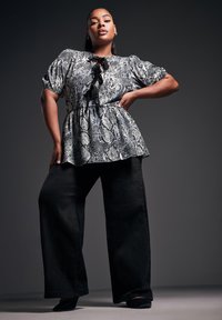 Top de estampado de serpiente en blanco y negro con mangas abullonadas y un lazo en el escote, combinado con pantalones de pierna ancha negros de talle alto.