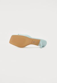 Una sandaletta con tacco di colore azzurro chiaro, con una parte superiore testurizzata, una forma ergonomica e una suola in gomma beige con linee orizzontali per una migliore aderenza.
