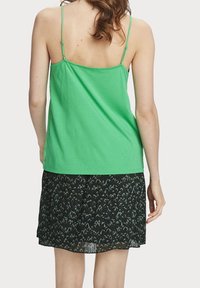 Vihreä puuvillainen toppi ohuilla olkaimilla, yhdistettynä mustaan hameeseen, jossa on teksturoitu kuvio. Hame on keskikokoinen ja laskostettu.