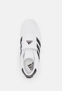 Vit Adidas-sko med ett mjukt läderöverdrag, detaljerad sömnad, tre svarta ränder och en vadderad tunga som har Adidas-logotypen.