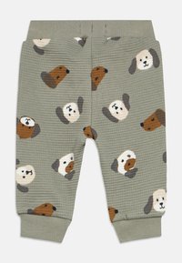 Grønne bukser med vaffeltekstur og spredte hundefacemønstre i brun og creme. Har elastisk taljebånd og tilspidsede manchetter.