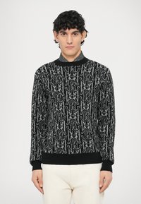 Maglione nero lavorato a maglia con un evidente motivo a logo grigio, collo, polsini e orlo a coste, con una silhouette aderente.
