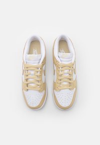 Nike-skor med ett vitt läderöverdrag och guldiga accenter, perforerat tåparti och platta snören. Texturerat material för bättre grepp.