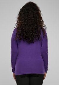 Langarmige paarse top gemaakt van zachte stof. Heeft een aansluitend ontwerp en een ronde halslijn, gecombineerd met donkere broek.