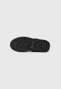 Suela de zapato de goma negra con superficie texturizada que presenta patrones triangulares y de diamante para mejorar el agarre y la tracción.
