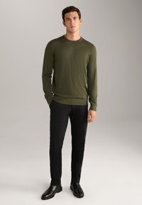 Olive green long-sleeve sweater with a crew neck, ribbed cuffs, and hem, paired with black trousers and black shoes. Smooth knit texture.